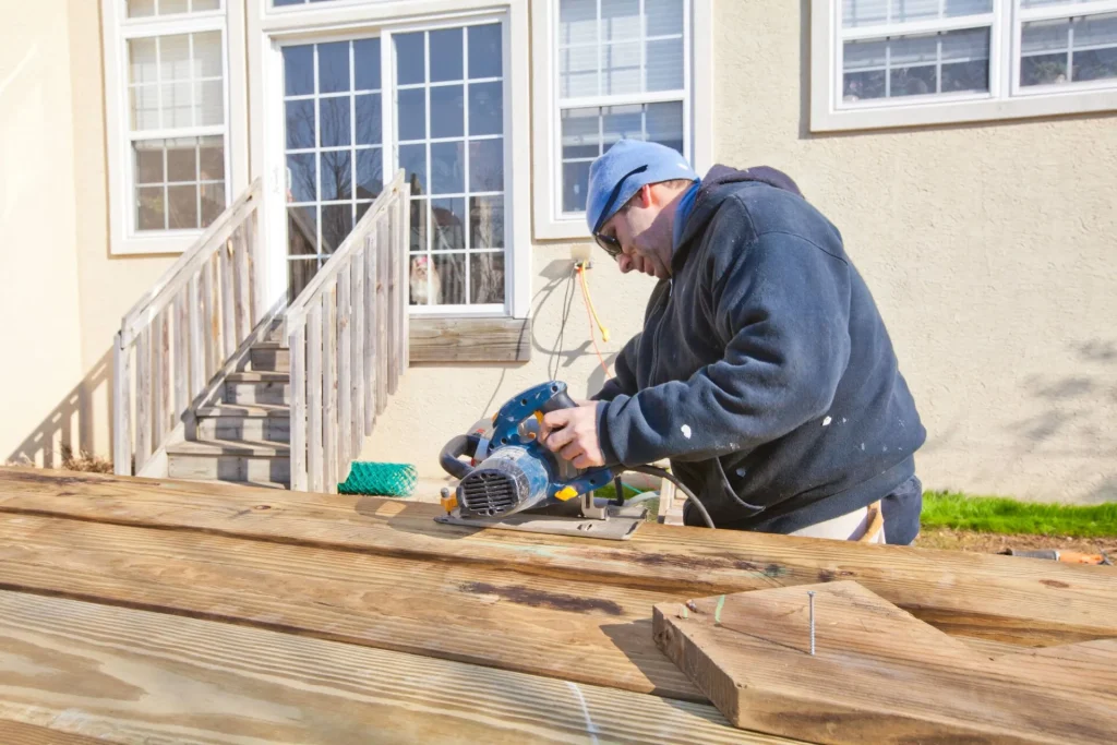 man sawing a wooden plank outside of a home