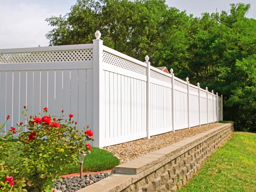 white vinyl fence on top of a retaining wall with red flowers next to it