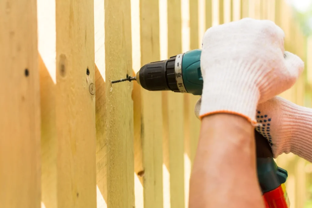 close up of pair of hands operating a power drill to drill into a wooden fence